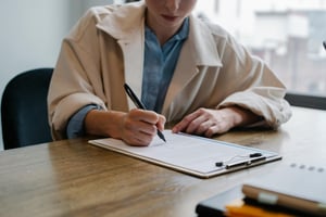 a women writing on a paper, sitting in a room