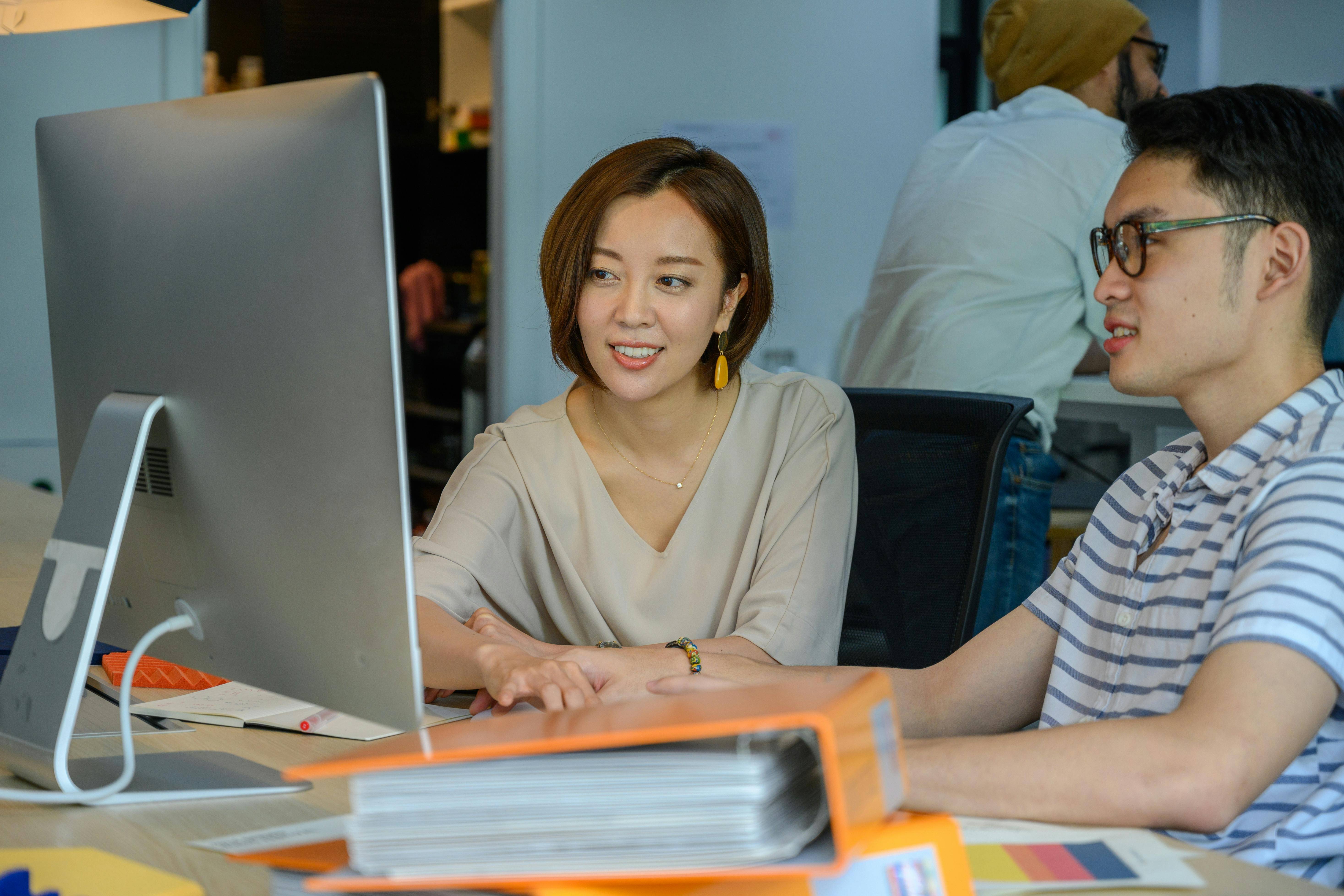 A man and woman seated at a desk, focused on a computer screen, engaged in a collaborative task.