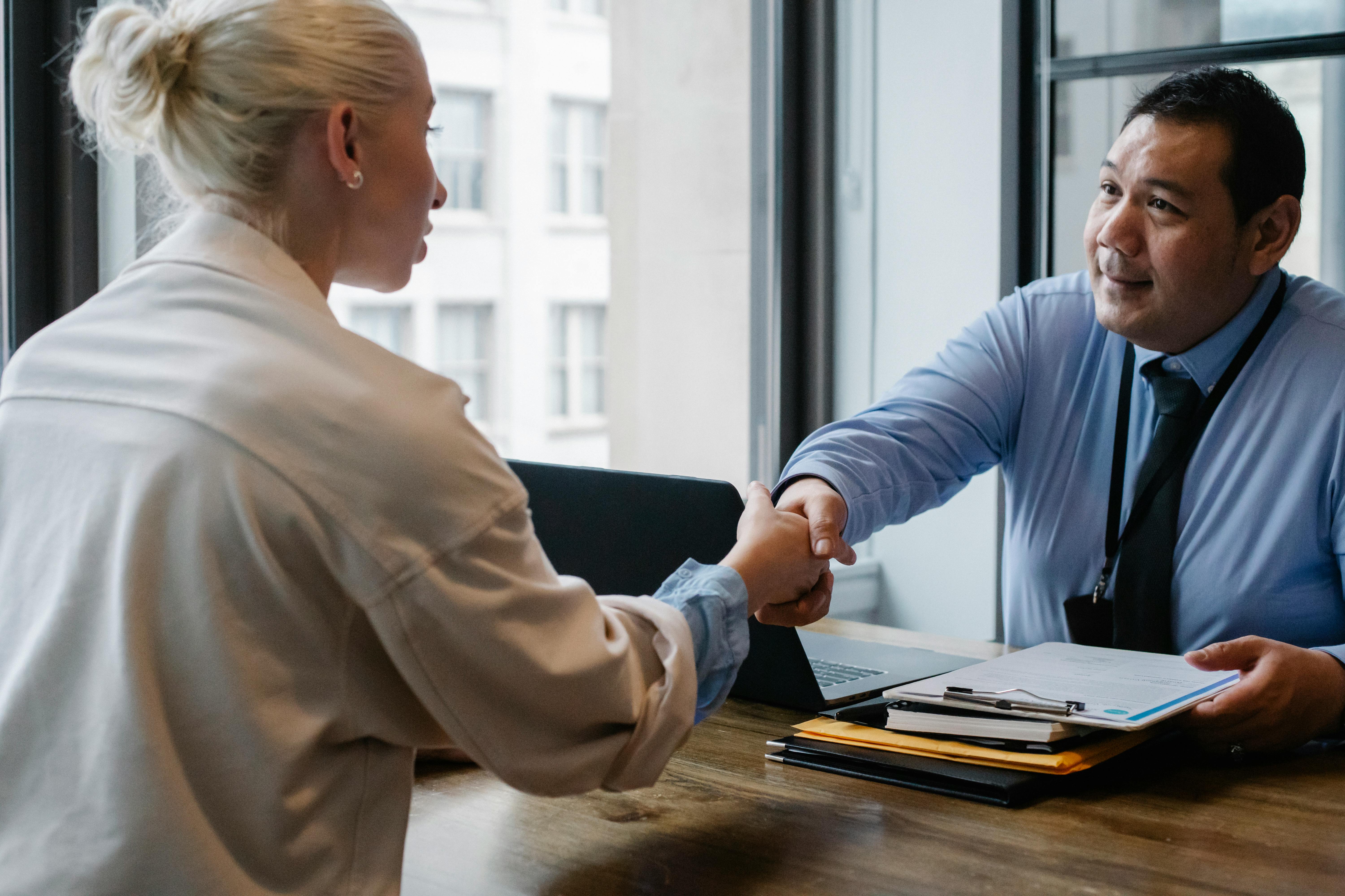 A man and woman shaking hands over a desk, symbolizing agreement and collaboration in a professional setting.