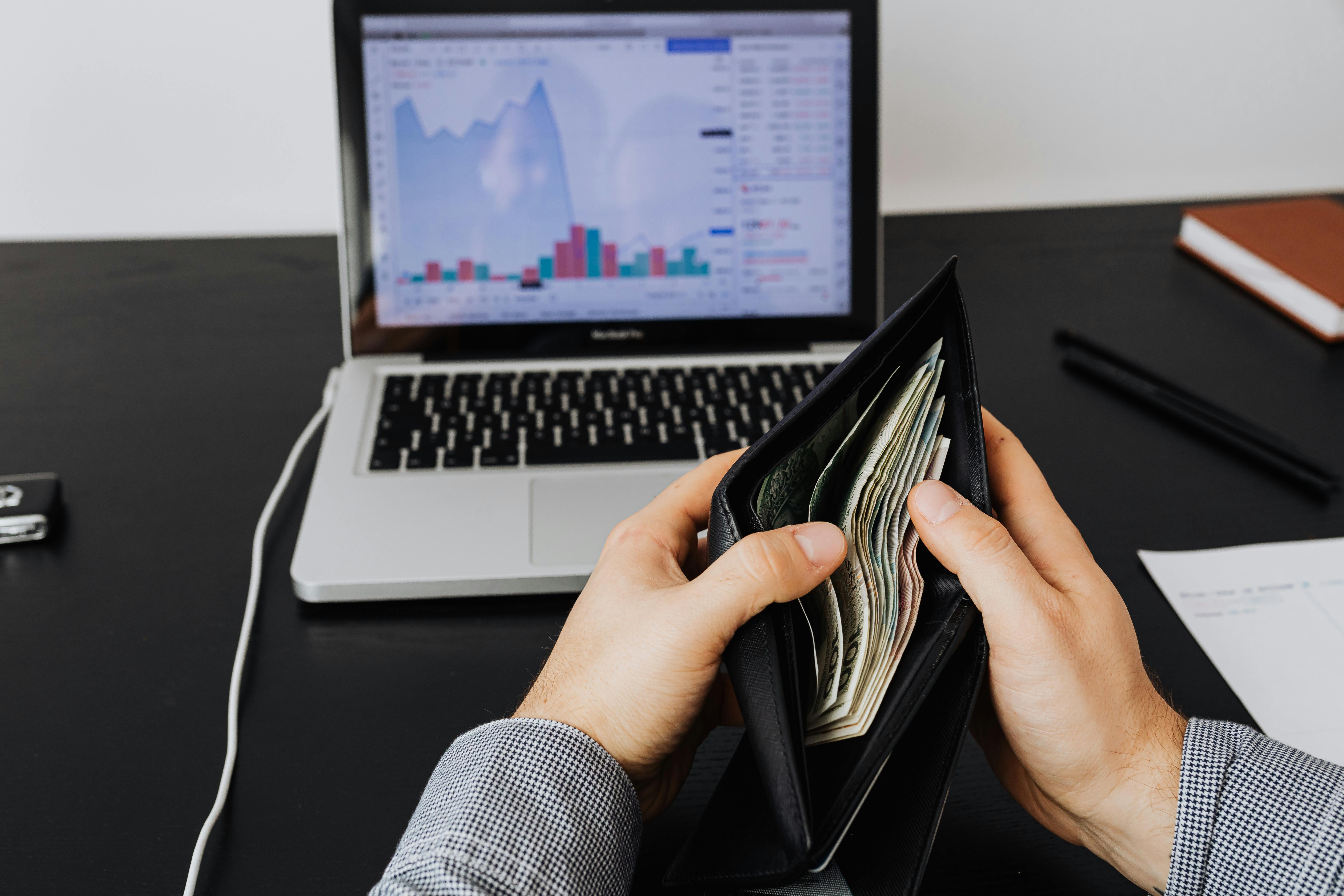 a laptop kept on desk, and a man showing money in his wallet