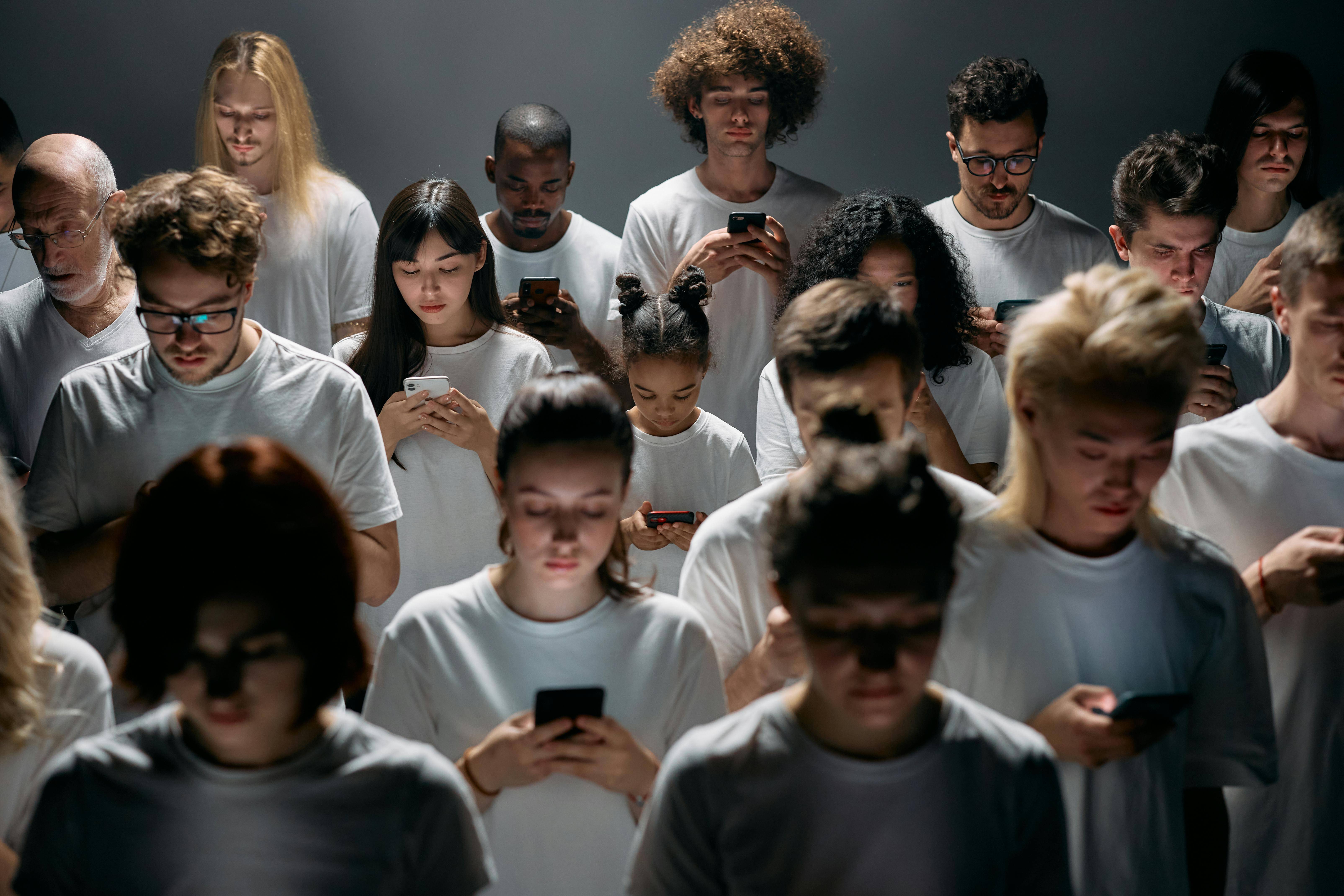 A group of individuals in white shirts are intently focused on their smartphones, engaged in their devices.